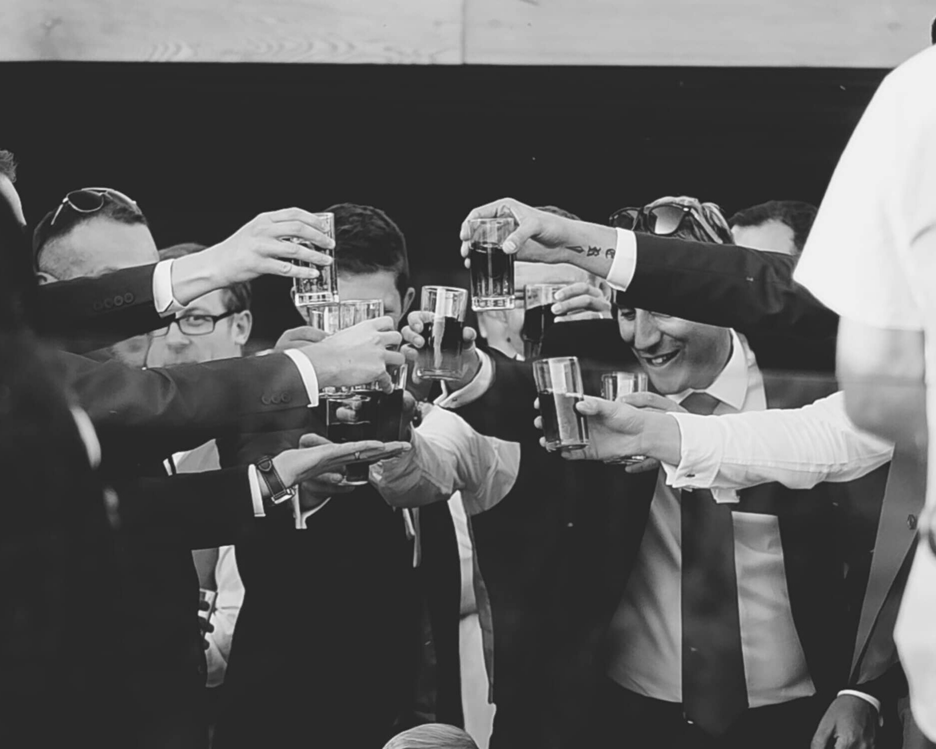 A group of people dressed in formal attire gather at The Boathouse, holding up glasses in a celebratory toast. The black-and-white image highlights the joyful mood and camaraderie during this private function.